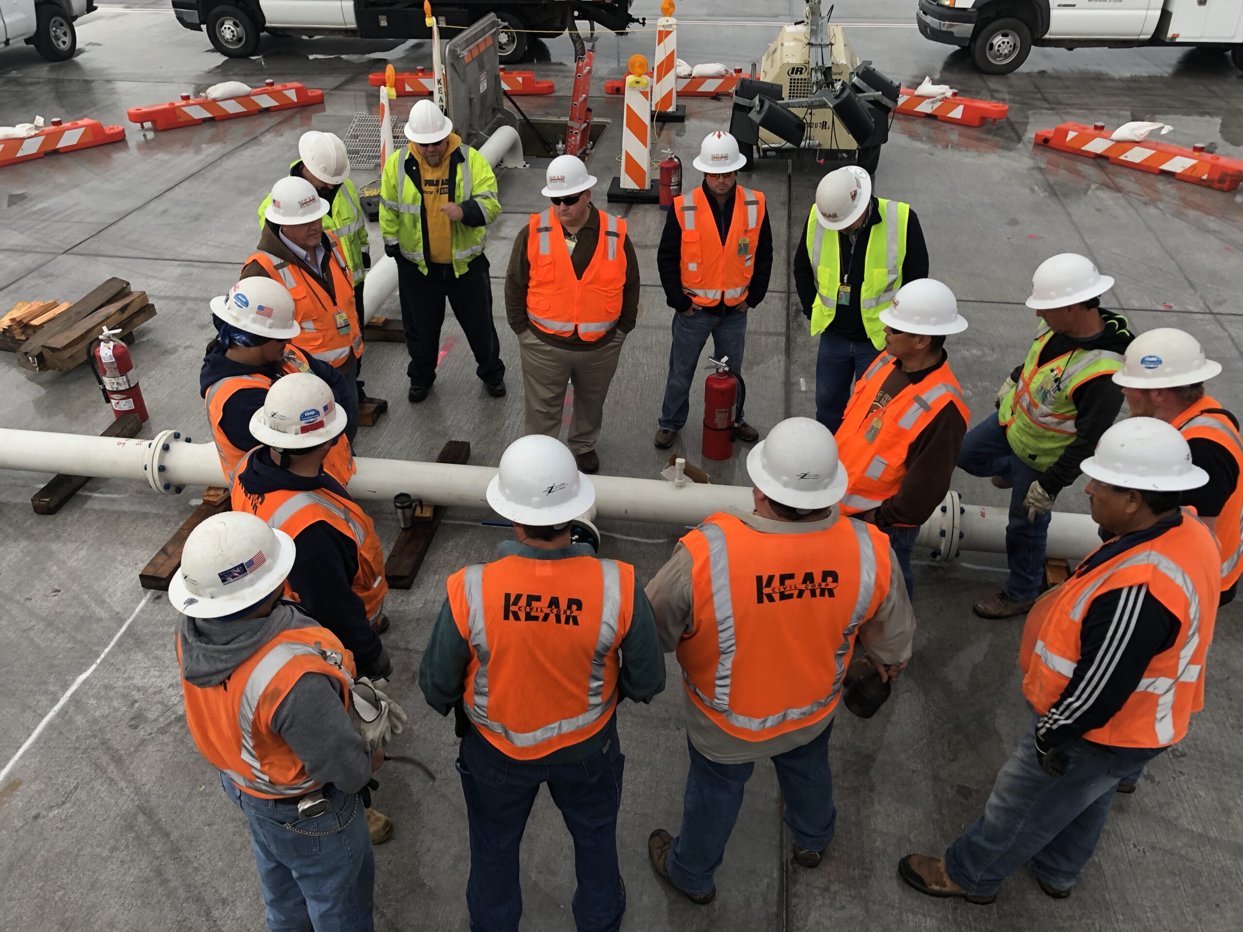 Group of construction workers in high-visibility vests and hard hats attending a briefing at an outdoor home construction site.