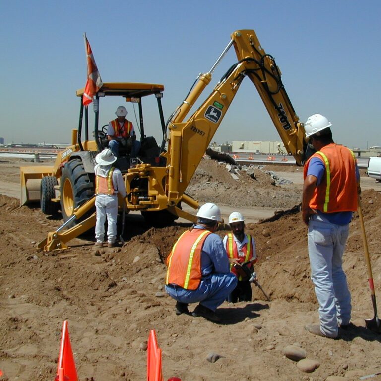 About construction workers in safety vests and helmets at a construction site with a backhoe in operation.