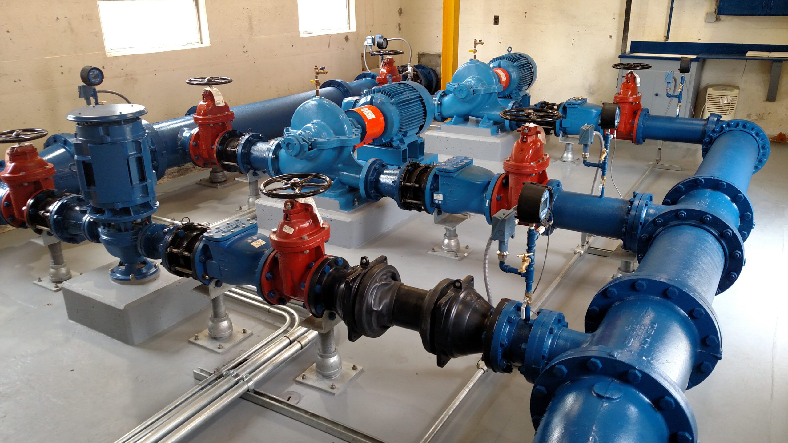 Industrial pump room with blue and red pipes, valves, and meters in a concrete building at Naval Base Point Loma.
