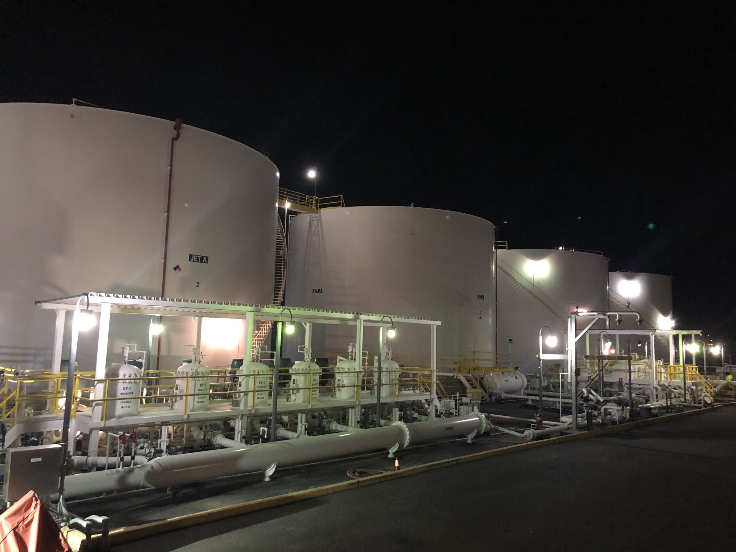 Large industrial tanks and piping illuminated at night at a chemical or fuel processing facility undergoing tank farm upgrades.