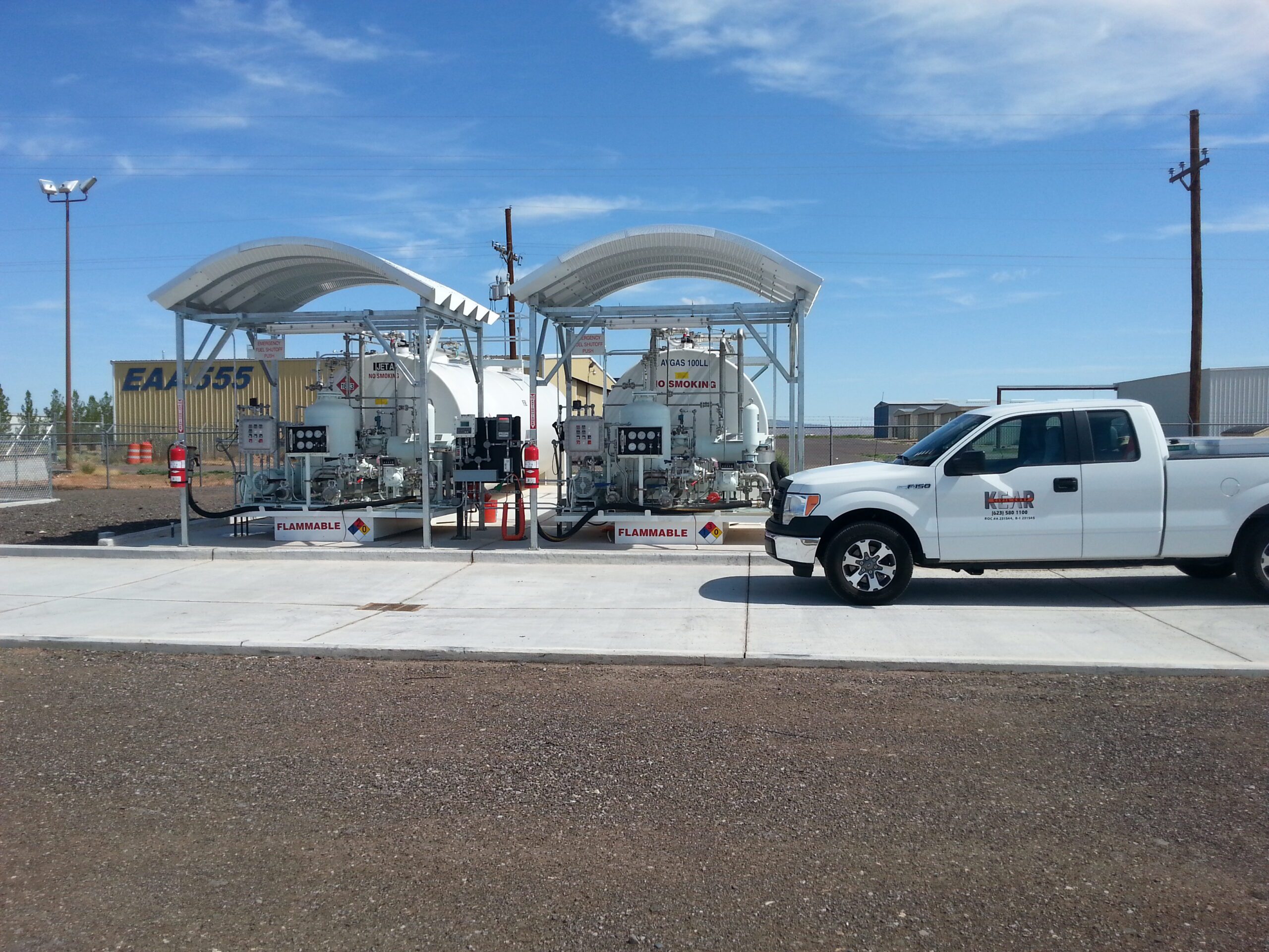 A white pickup truck parked at the New Mexico Fuel Farm with multiple pumps under canopies, displaying various flammable signs.