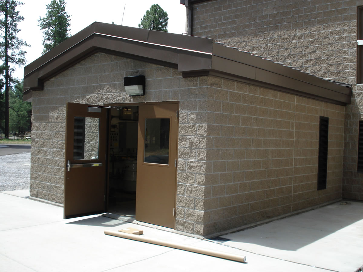 An exterior view of a beige stone building at the Lake Mary Water Treatment Plant with an open door, featuring a brown roof and a small window.