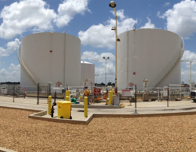 Two large white storage tanks at Memphis International Airport in an industrial area with various pipes and valves in the foreground, under a cloudy sky.