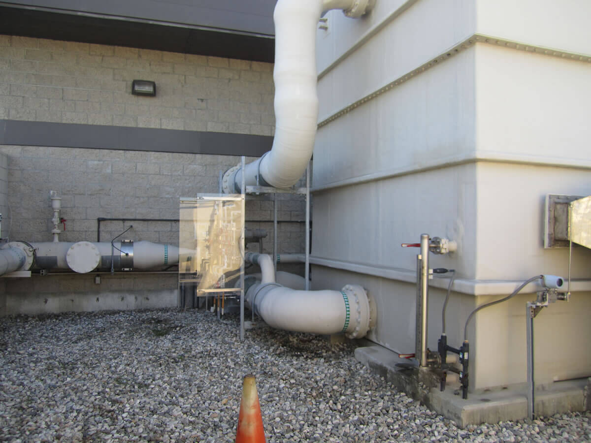 Exterior view of a building's utility setup in Torrance CA, with large pipes and a weather shielded equipment casing on a gravel bed.