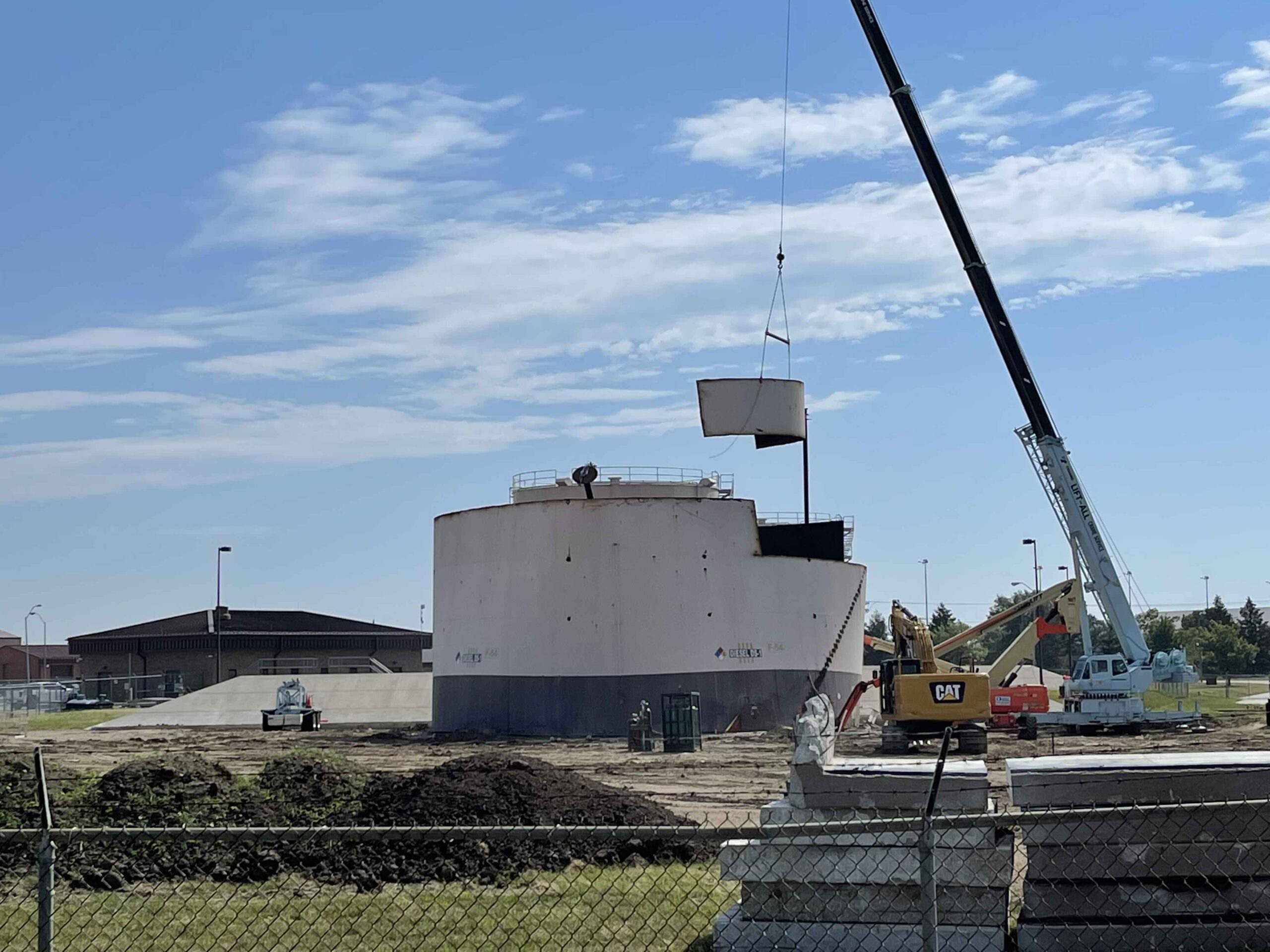 A large, cylindrical storage tank is being hoisted by a crane at Offutt Air Force Base under a clear sky.