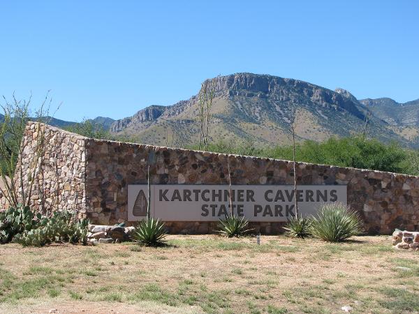 Entrance sign of Kartchner Caverns State Park with a mountain backdrop under a clear blue sky.