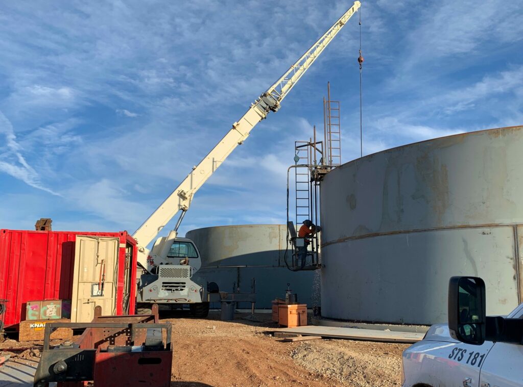 A construction site with a crane near large storage tanks in Prescott Valley, workers on site, and various construction vehicles and equipment.